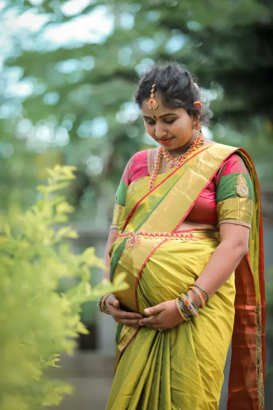 Expectant mother in a golden silk saree and temple jewellery cradling her baby bump