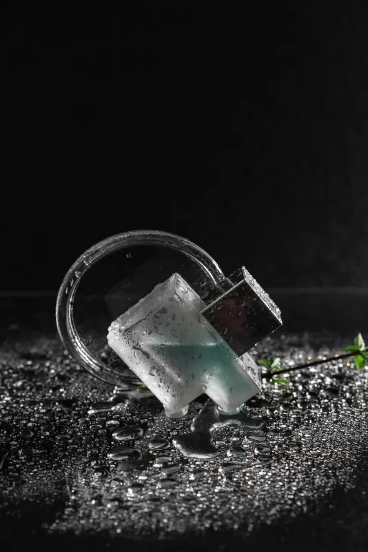 Frosted glass perfume bottle with a silver cap lying in water droplets on black