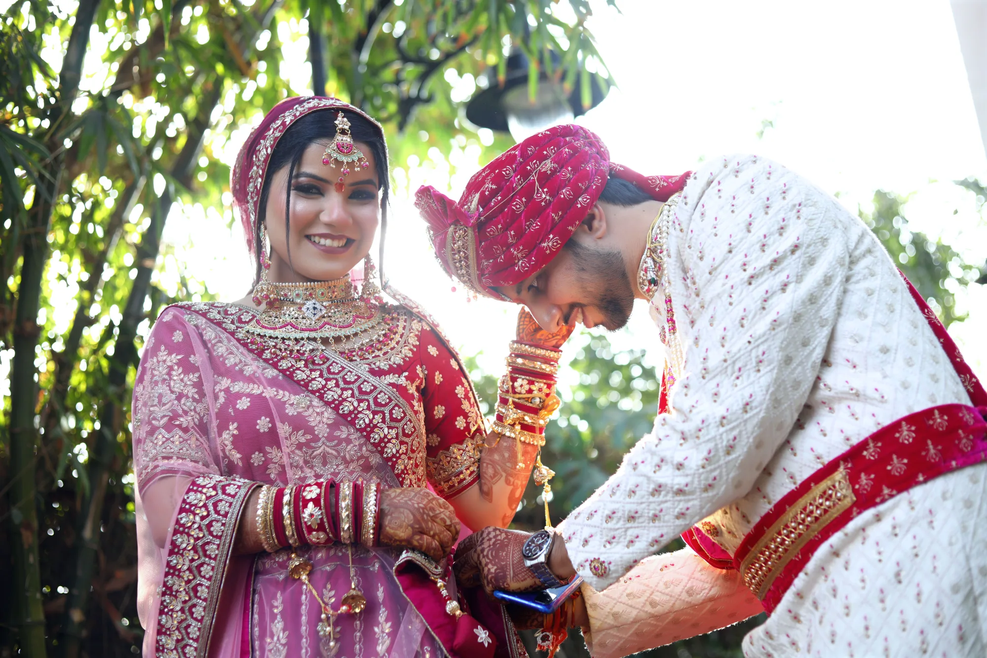 Indian bride and groom in traditional red and cream wedding attire adorned with floral garlands during ceremony